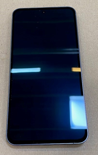 Przód smartfona. Czarny ekran, złota ramka. Wyświetla ciemny obraz. Jasne tło.