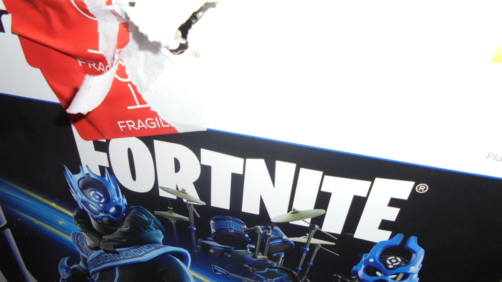 Rozerwana skrzynka z logo Fortnite i grafiką zestawu perkusyjnego, widoczna czerwona etykieta 'FRAGILE'.