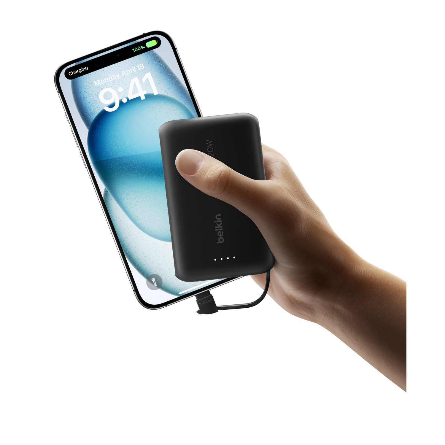 Une main tient une batterie externe Belkin noire qui charge un téléphone. Le téléphone affiche 100% de charge.