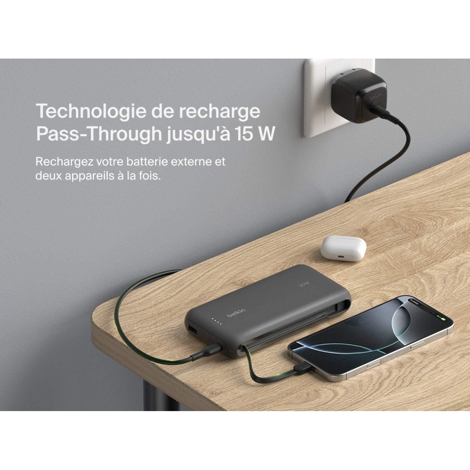 Power bank Belkin chargeant depuis prise murale et chargeant iPhone. Un étui AirPods blanc est aussi sur la table.