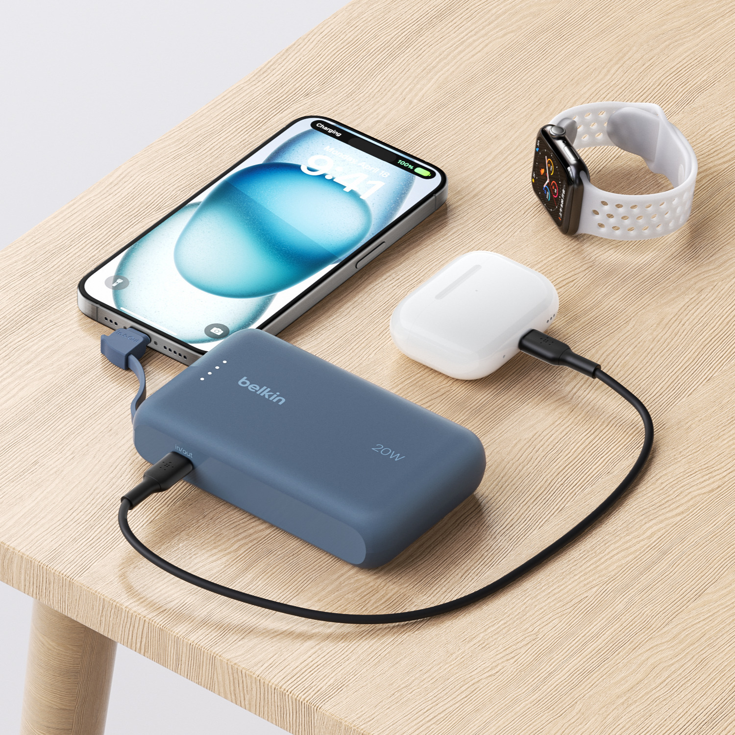 Téléphone, montre, écouteurs et une batterie externe Belkin sur bois.