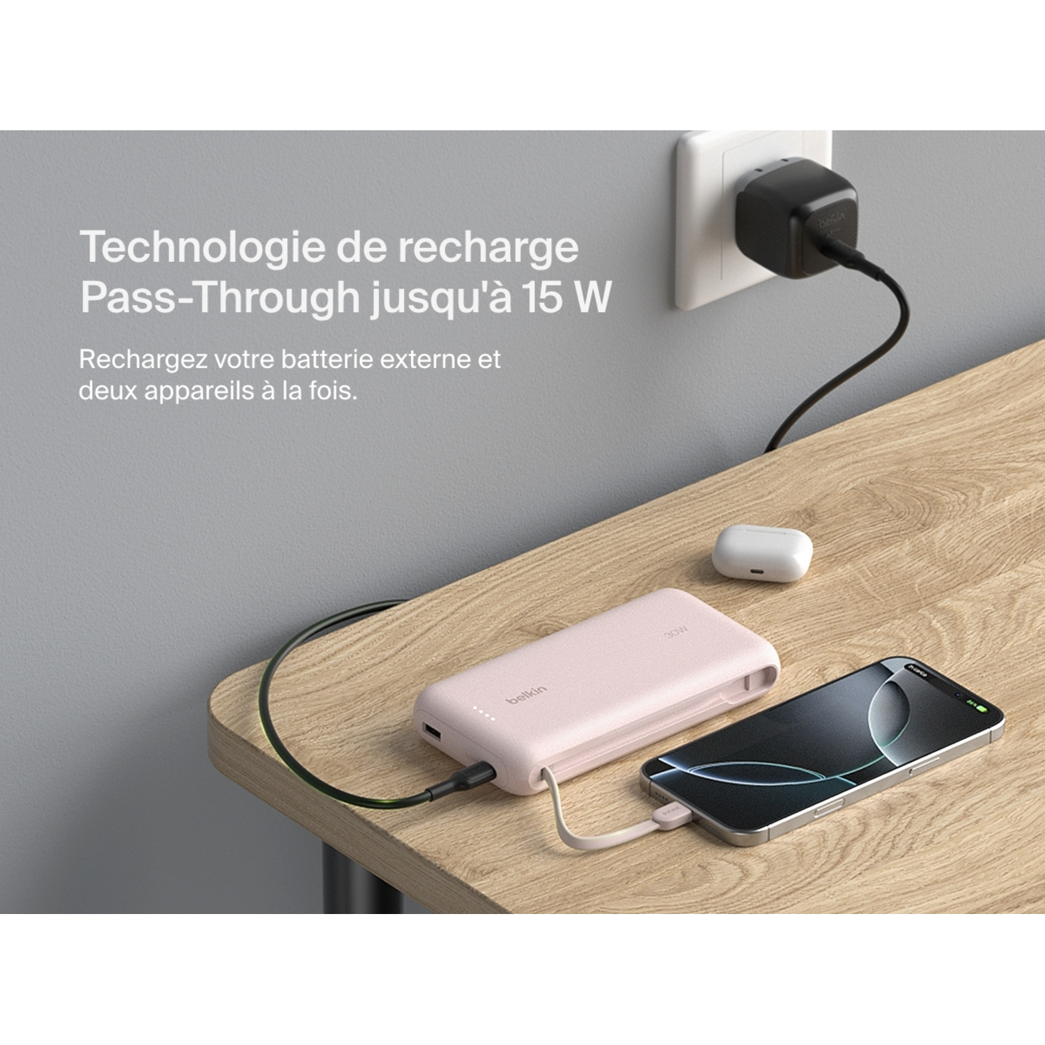 Batterie externe Belkin rose et téléphone sur une table. Chargeur branché. Fond blanc.