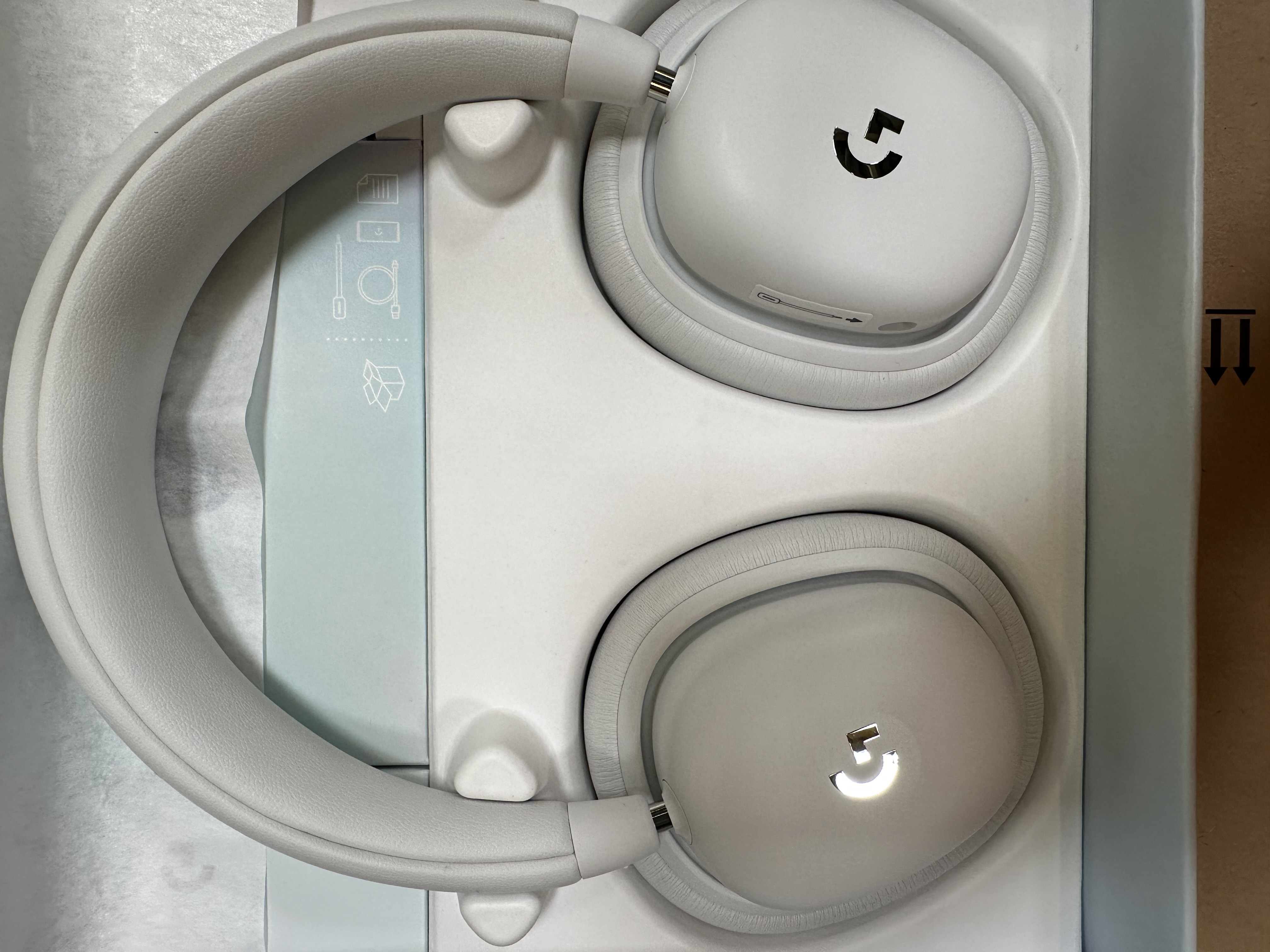 Białe słuchawki Logitech w opakowaniu. Muszle, pałąk widoczne. Czarne logo 'G'.