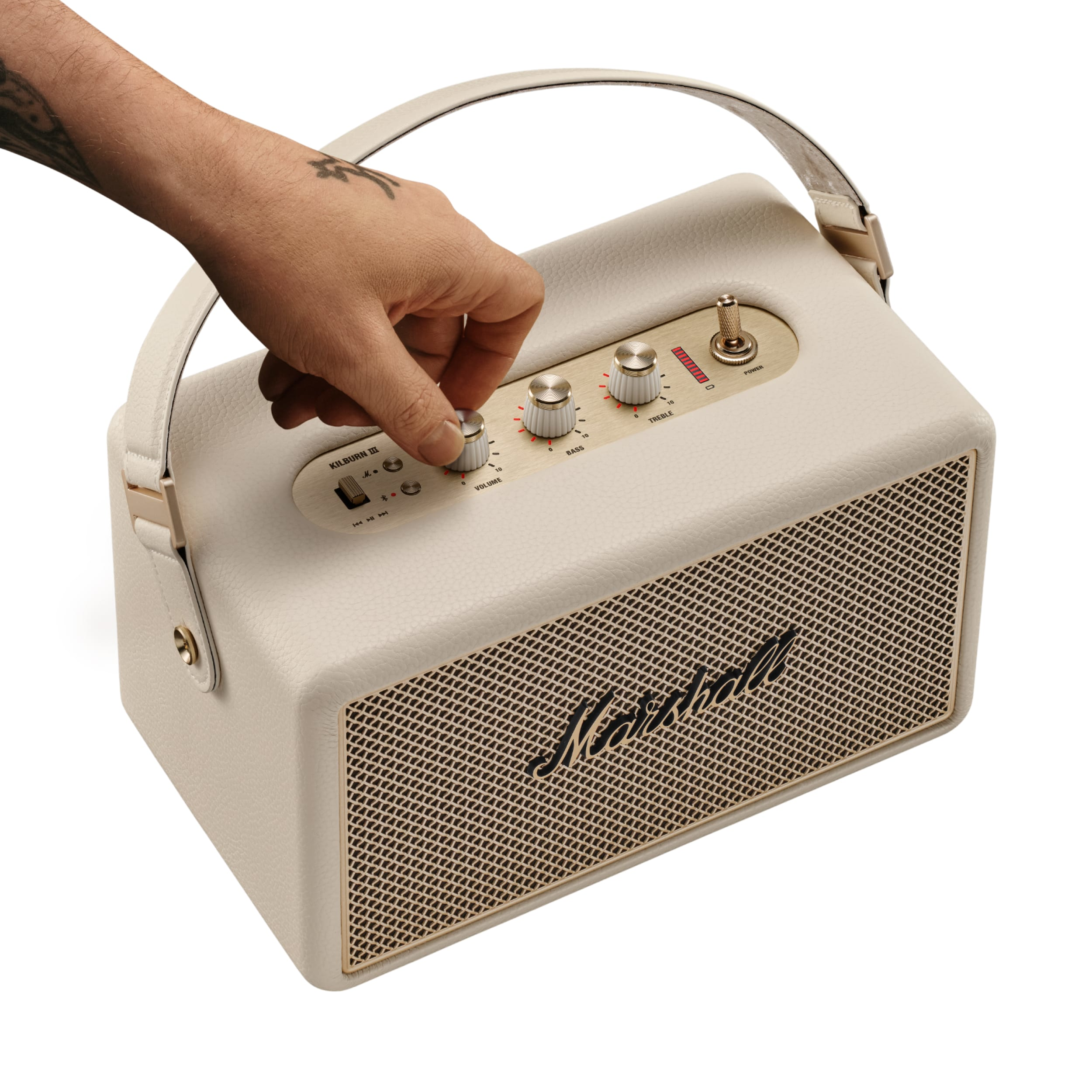 Eine Hand stellt den Lautstärkeregler an einem cremefarbenen Marshall-Lautsprecher ein. Logo sichtbar. Weißer Hintergrund.