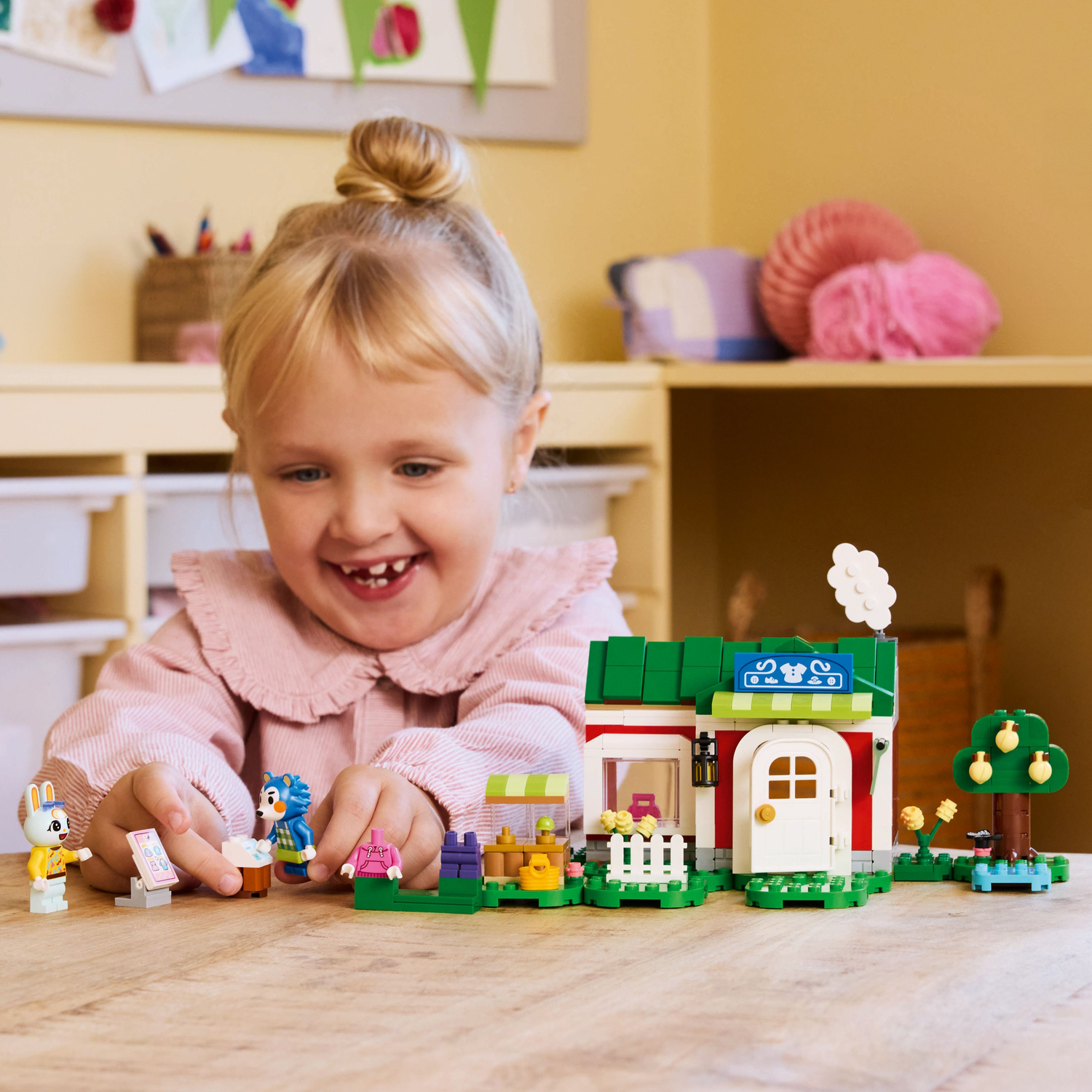 Child playing with LEGO Animal Crossing set on a table. The set includes figures and a shop.