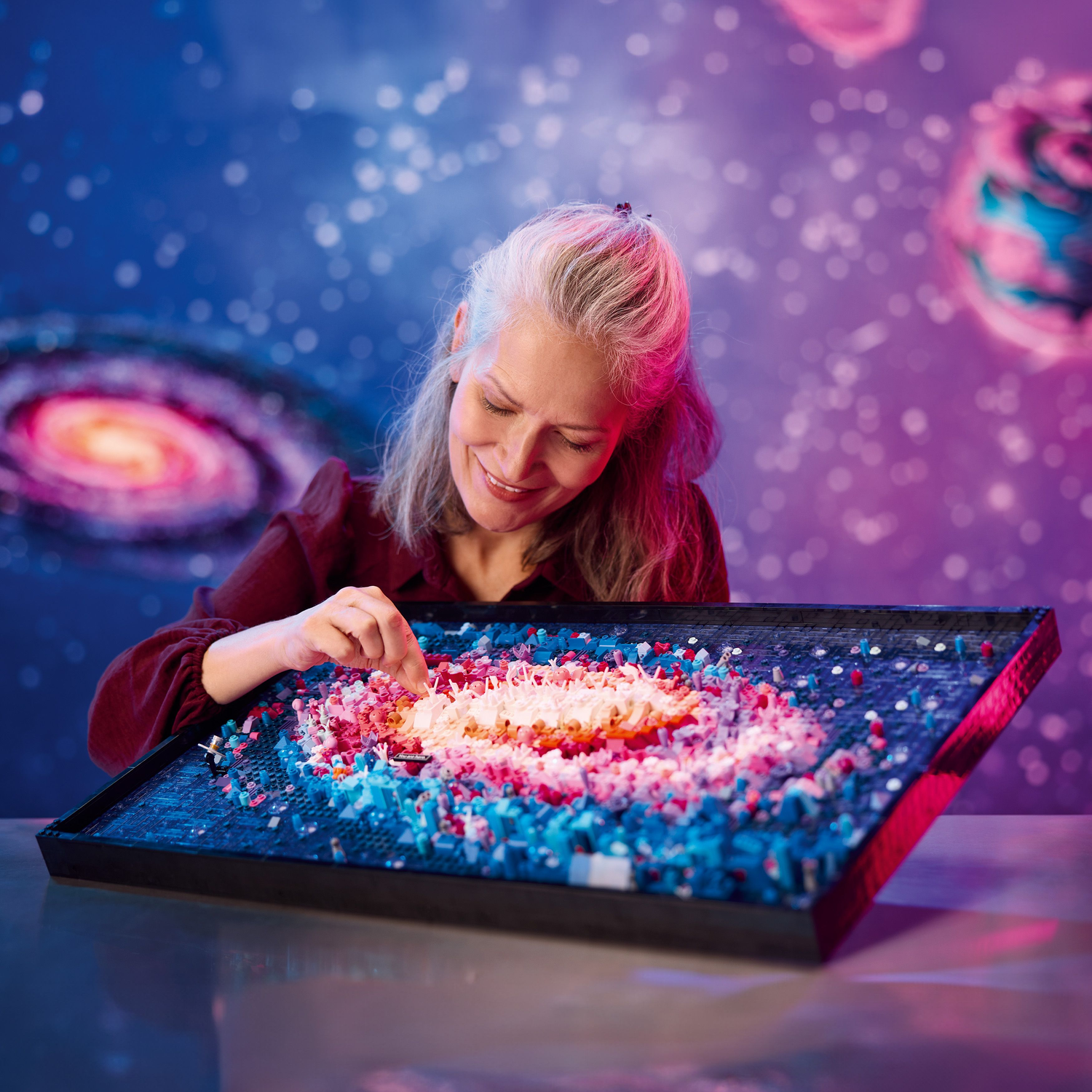 Een vrouw die een Lego Melkweg kunstwerk in elkaar zet, glimlachend.