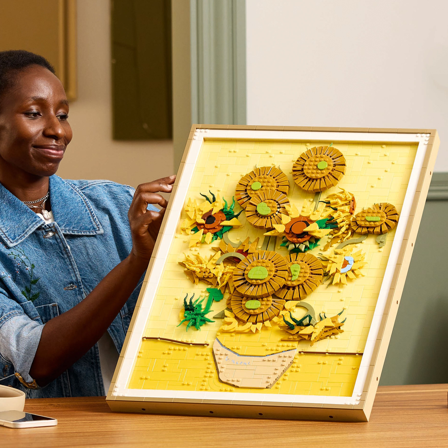 Vrouw houdt LEGO zonnebloemen kunstwerk vast, ingelijst, toont de LEGO set en zonnebloemen.