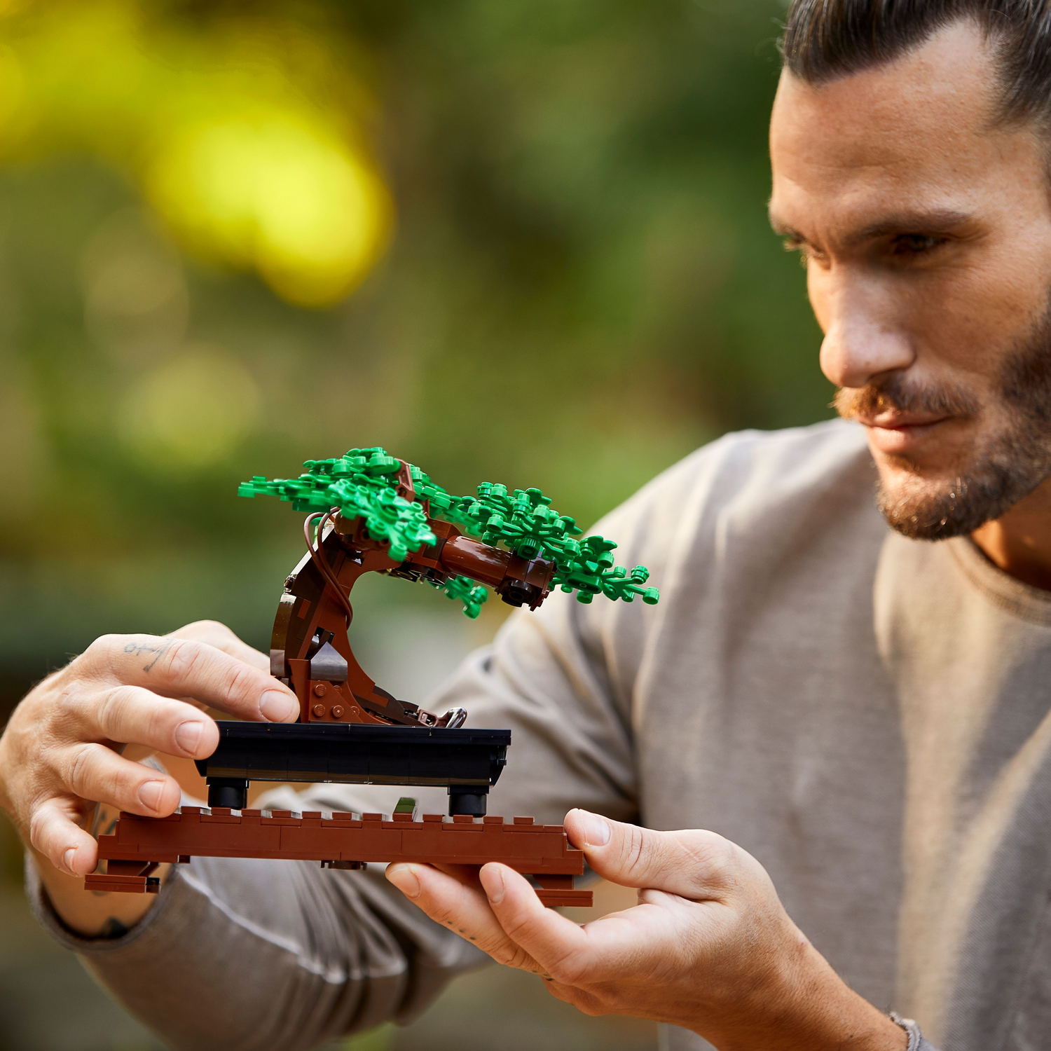 Man met lego bonsai boom. Een man met een lego bonsai boom op een houten standaard.