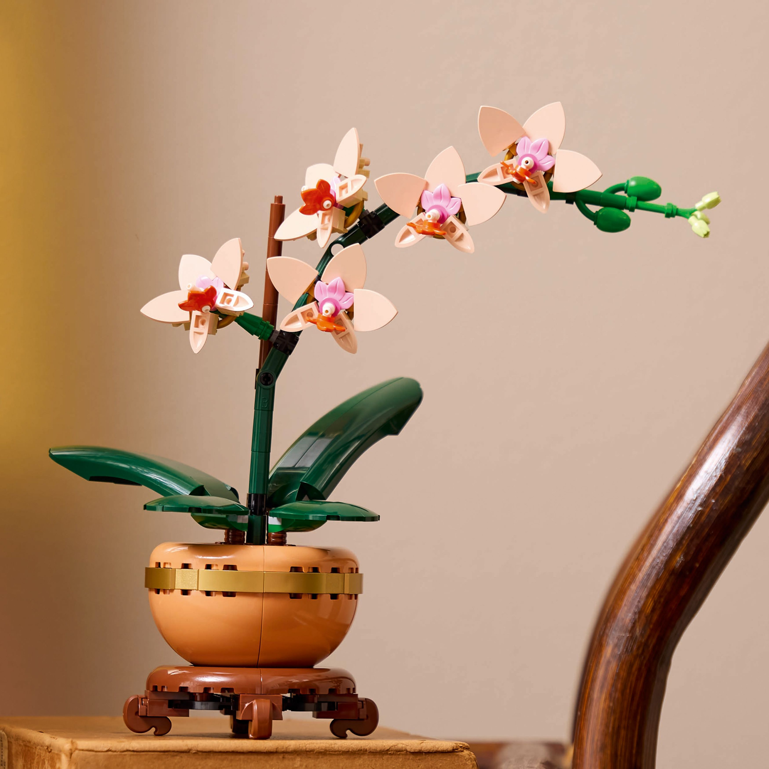Lego Mini Orchid in a pot on a wooden stand.  The background is a light-colored wall and a wooden chair.