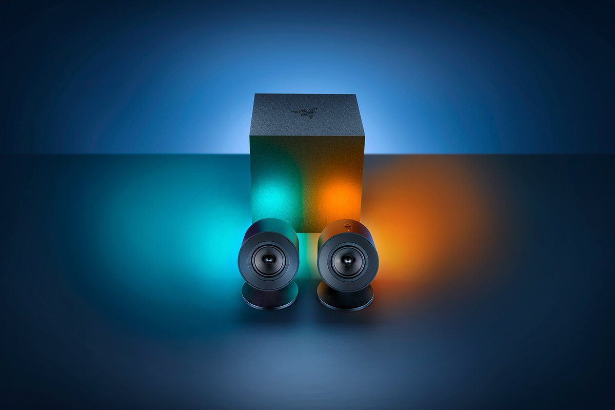 Dwa czarne głośniki gamingowe Razer i subwoofer, oświetlone niebieskim i pomarańczowym światłem.