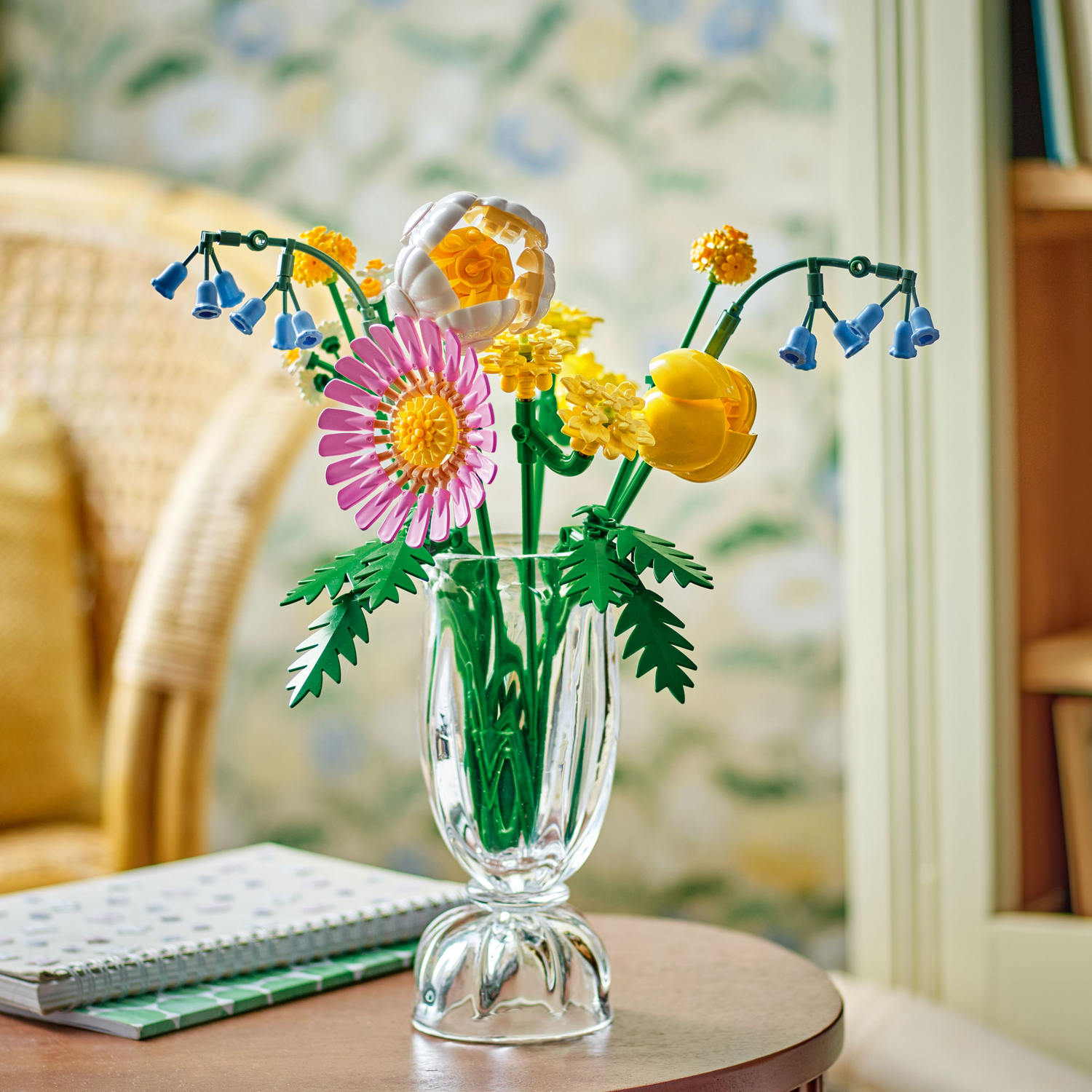 A Lego flower bouquet in a glass vase on a table. Flowers include pink, yellow, and blue Lego elements.