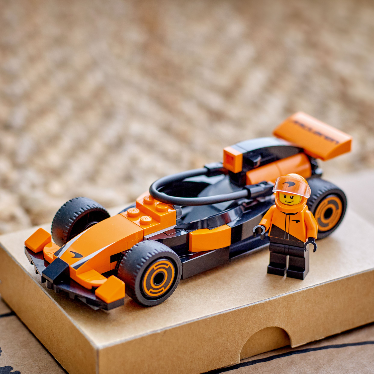 A Lego race car and driver standing on a cardboard box.