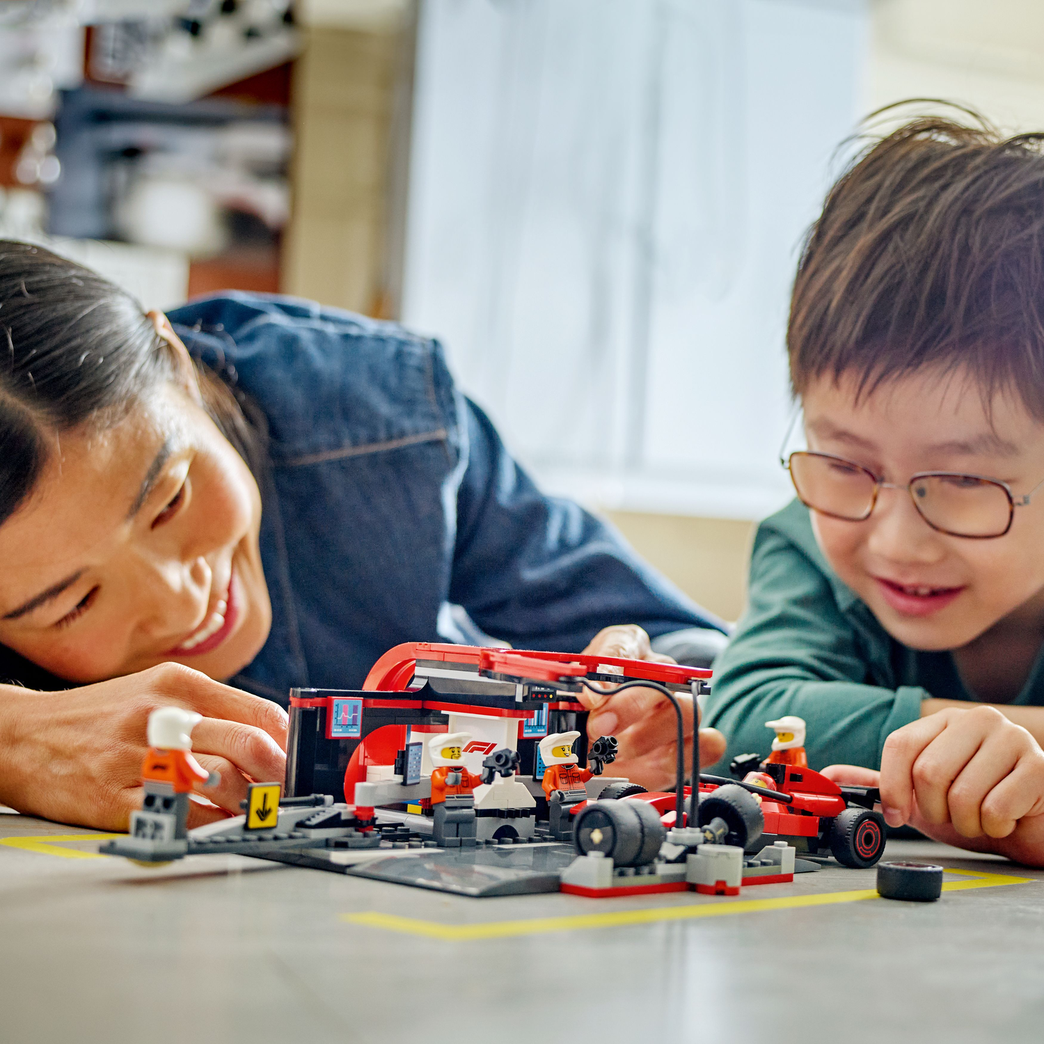 A mother and child building a LEGO F1 set together, with a yellow marker on the floor.