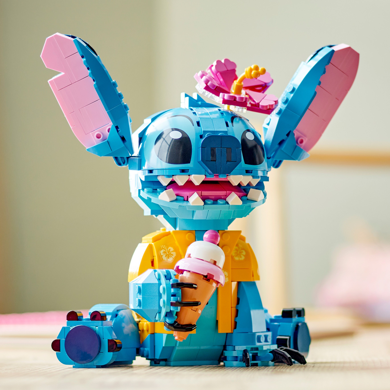 Lego Stitch figuur met ijs. Zittend. Blauw met roze oren en bloem. Lichte achtergrond.