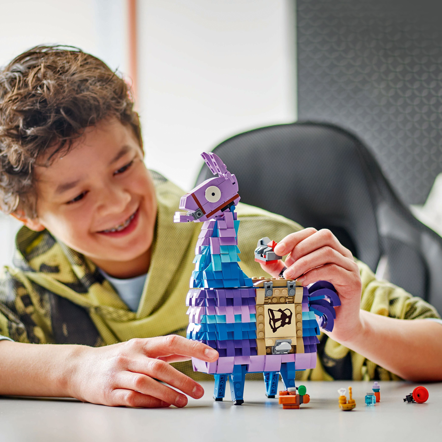 A boy is playing with a LEGO Fortnite Llama model. He is smiling.