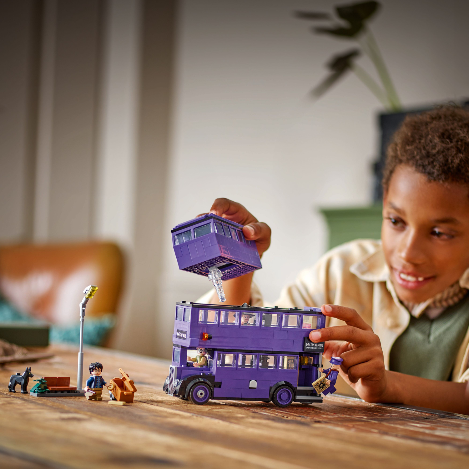 A child assembling a LEGO Knight Bus model, with the bus and minifigures on a table.