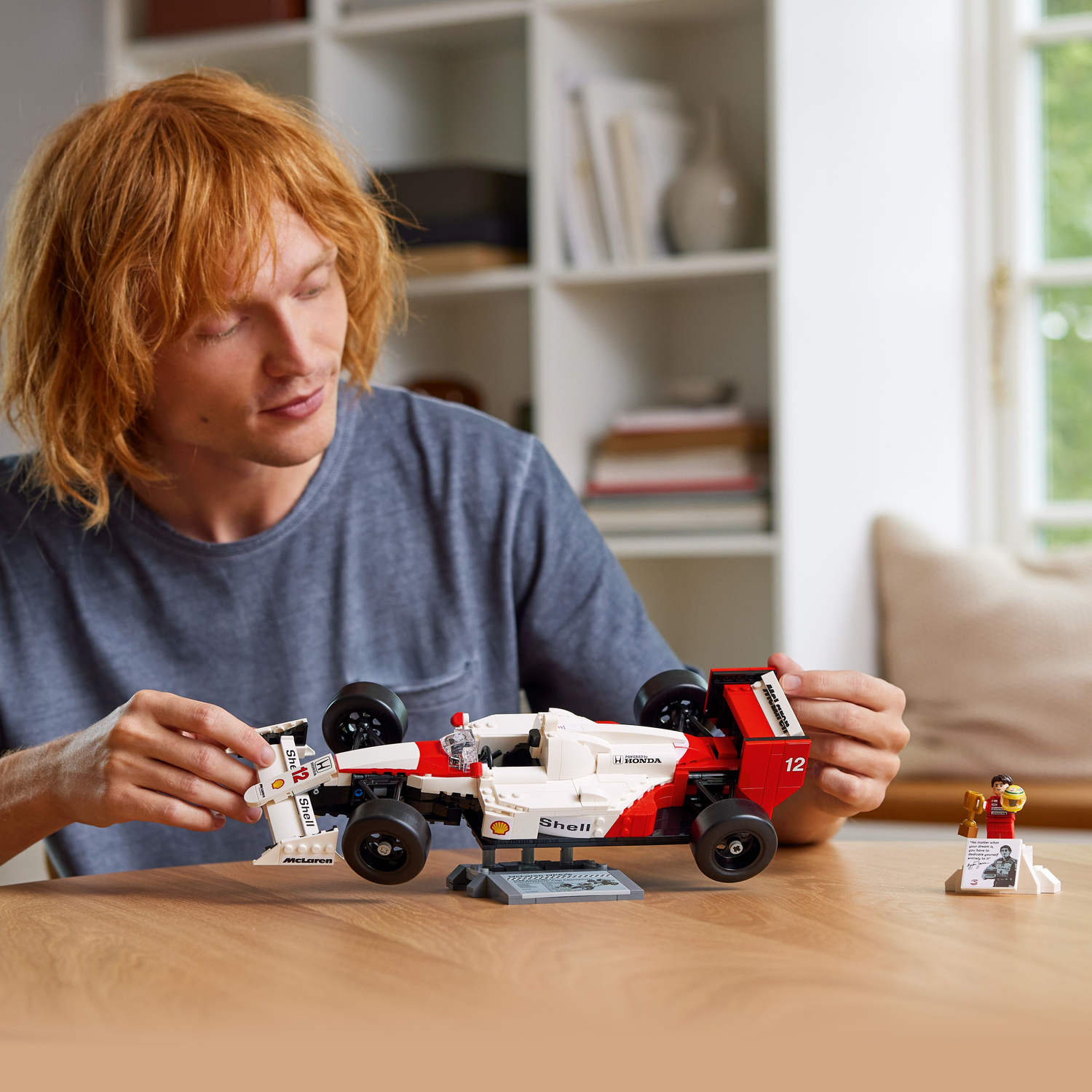 Man die een Lego McLaren raceauto in elkaar zet. Het model is wit en rood. Er is een beeldje en trofee.