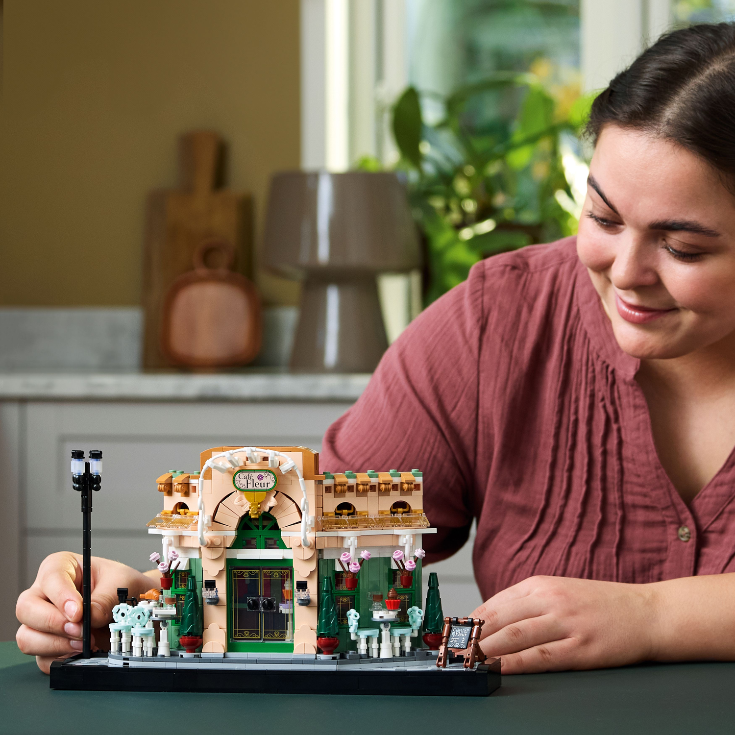 A woman assembles the French Cafe LEGO model, focusing on the building and a streetlight.
