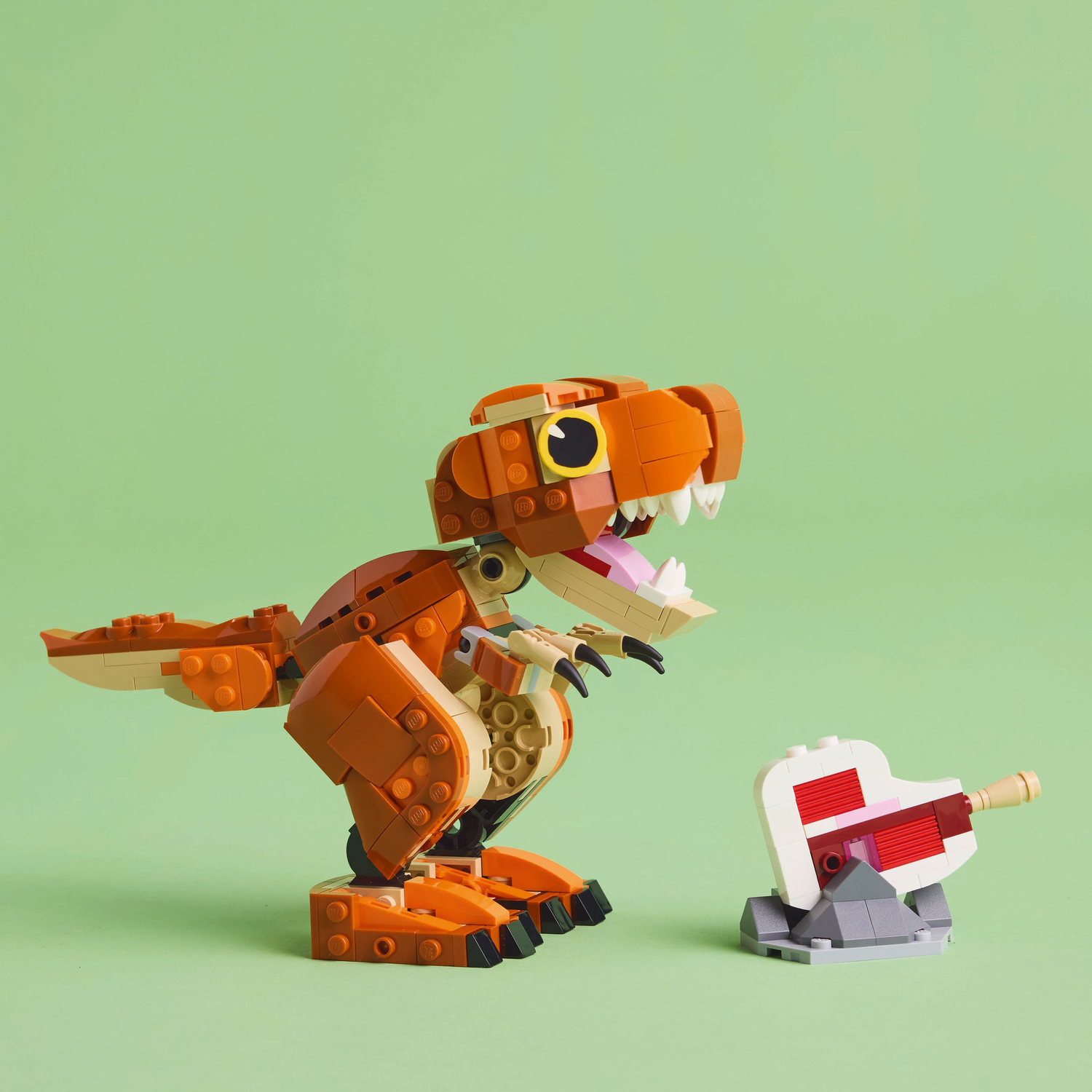 Een oranje Lego T-rex dinosaurus speelgoed staat voor een wit taart speelgoed met roze glazuur op groen.