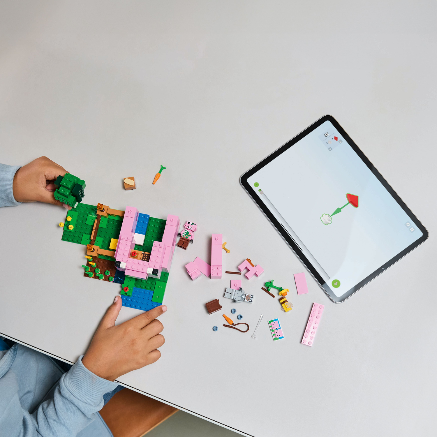 Handen die een Lego Minecraft set in elkaar zetten op een witte tafel naast een tablet.