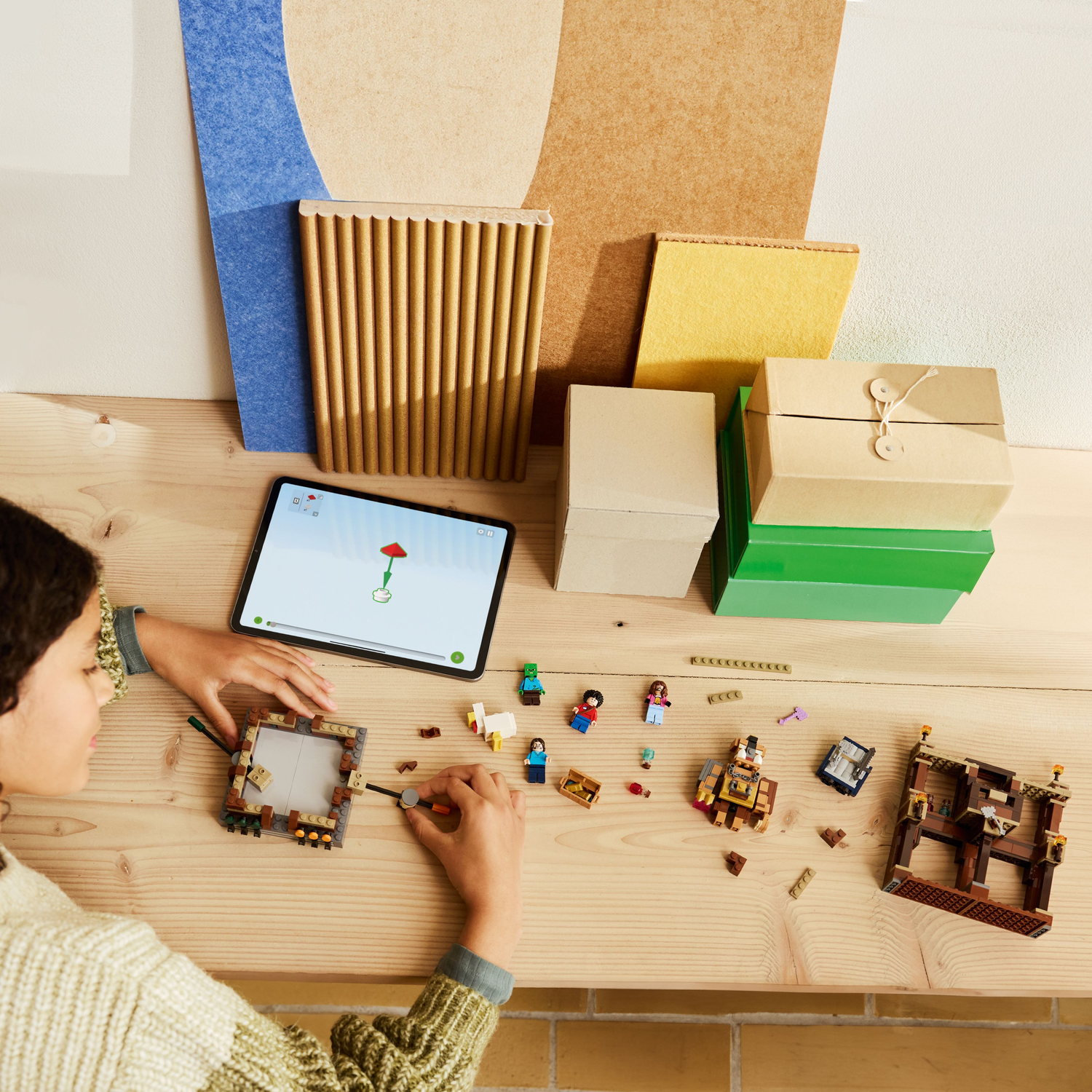 A person building a Lego set of a structure with blocks and figures on a wooden surface. Many boxes around.