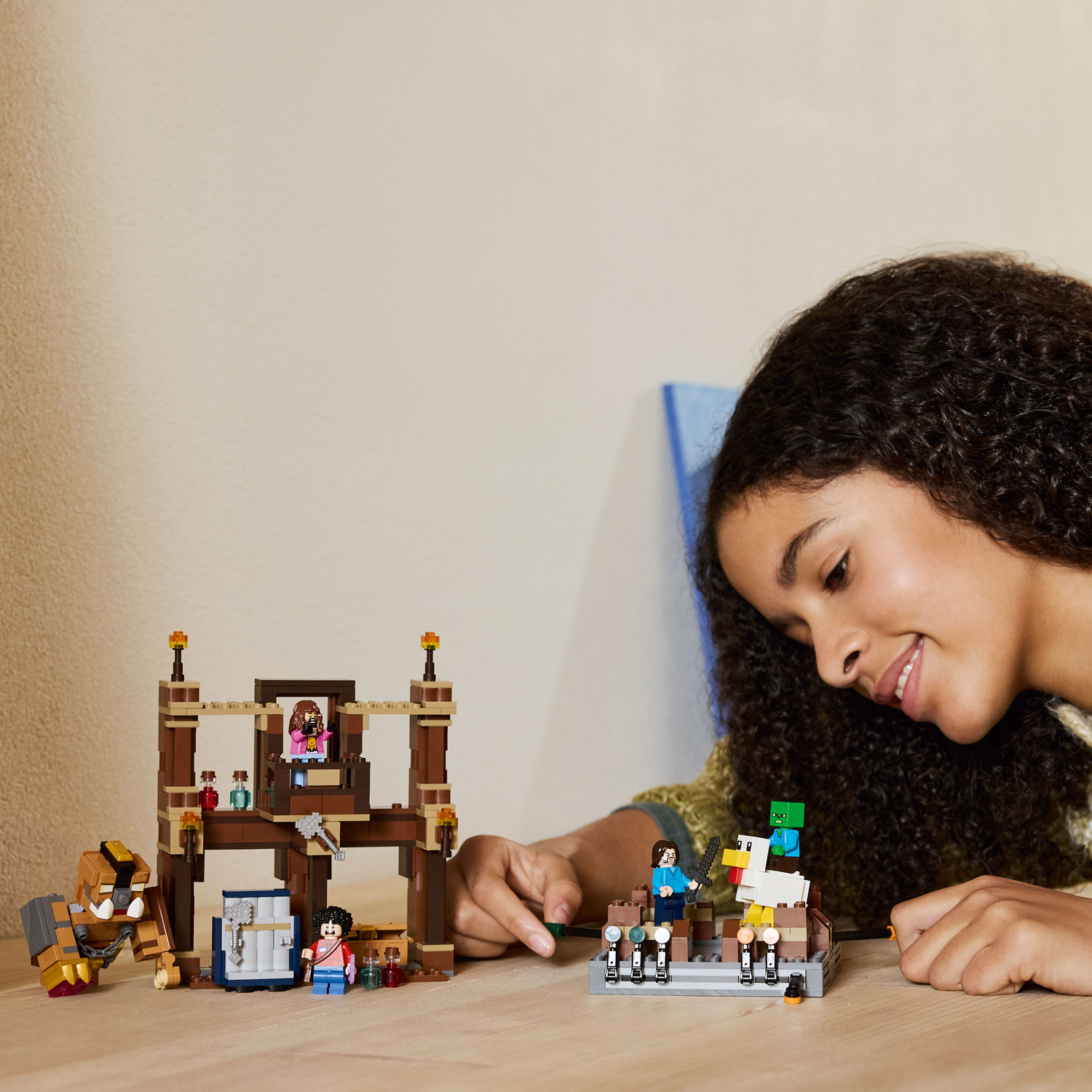 A girl looking at a Lego set that includes a tower and a fighting ring with Lego figures on a wooden surface.