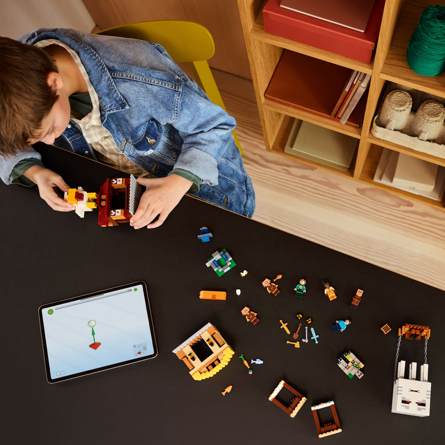 Een kind bouwt een Lego Minecraft set met een tablet met instructies. Set onderdelen en figuren liggen op de tafel.