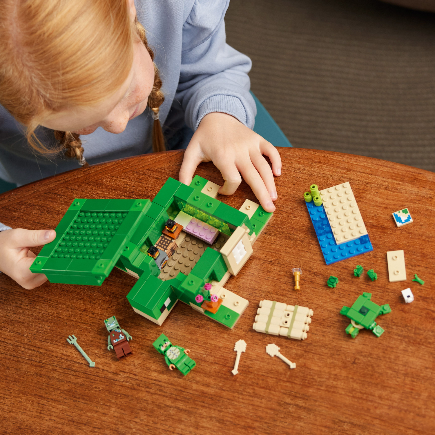 Een kind bouwt een Lego Minecraft schildpaddenhuis. Onderdelen, figuren en een half afgebouwd huis op een tafel.