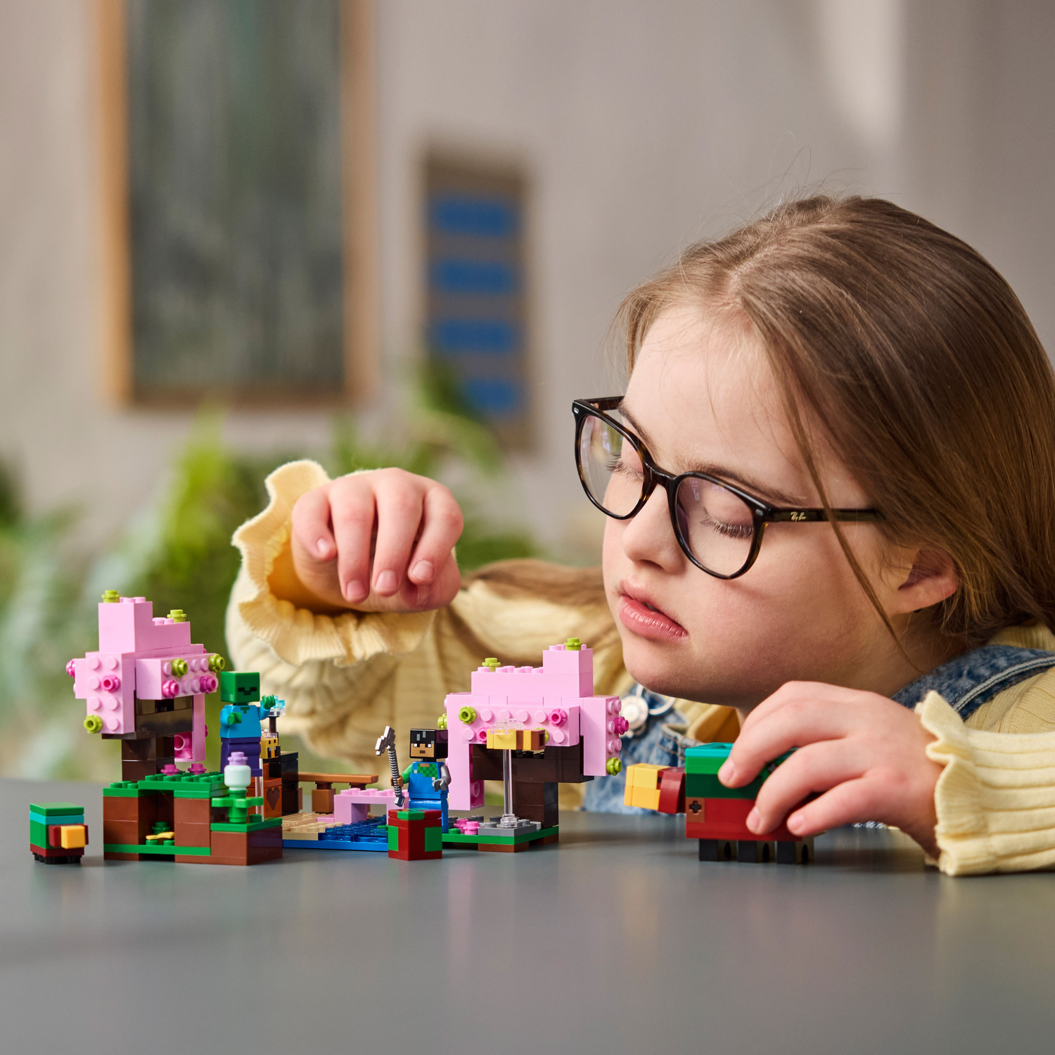 Een kind bekijkt een Lego Minecraft set, met verschillende figuren en structuren op de tafel.