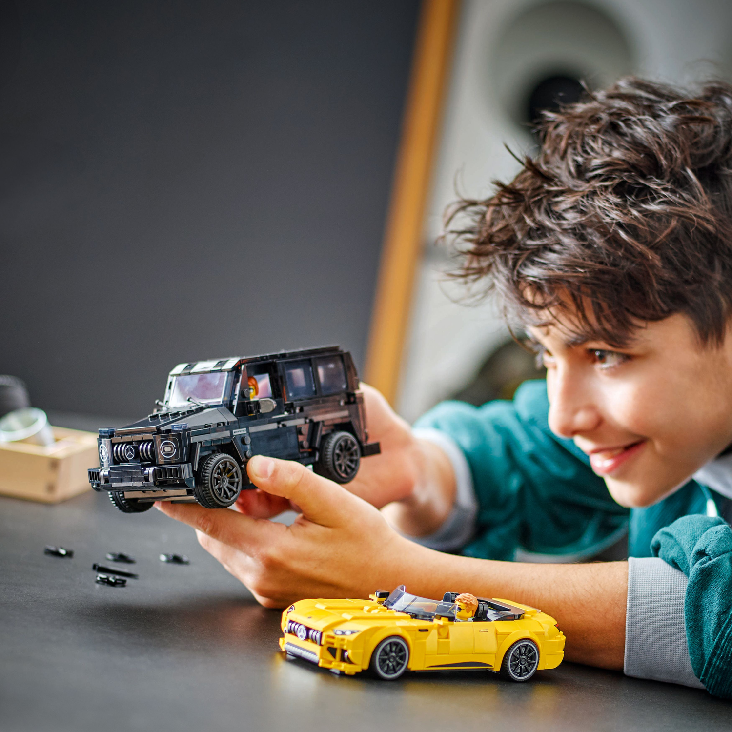 Een jonge jongen met een Lego set in zijn handen met een zwarte SUV en een gele auto.