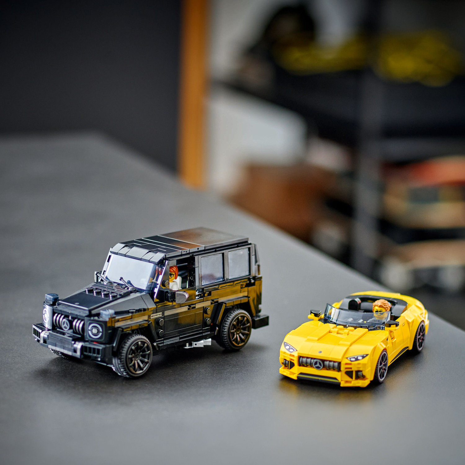 Een zwarte SUV en een gele auto worden op een grijze tafel getoond. De achtergrond is wazig.