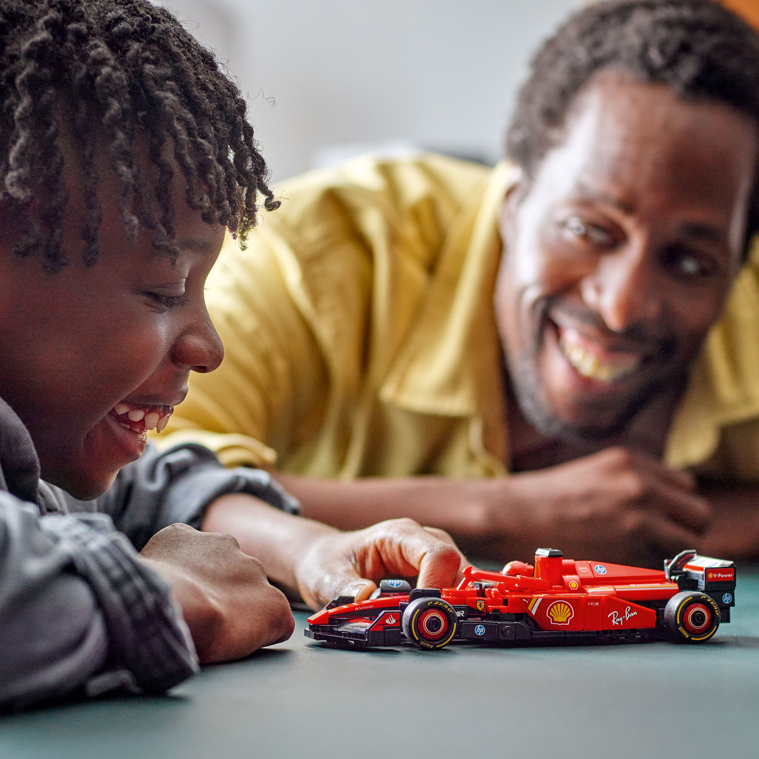 Father and son playing with a red Ferrari F1 LEGO car on a table.
