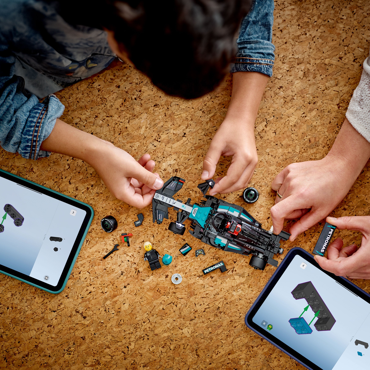 People building a black LEGO Mercedes F1 car with instruction tablets.