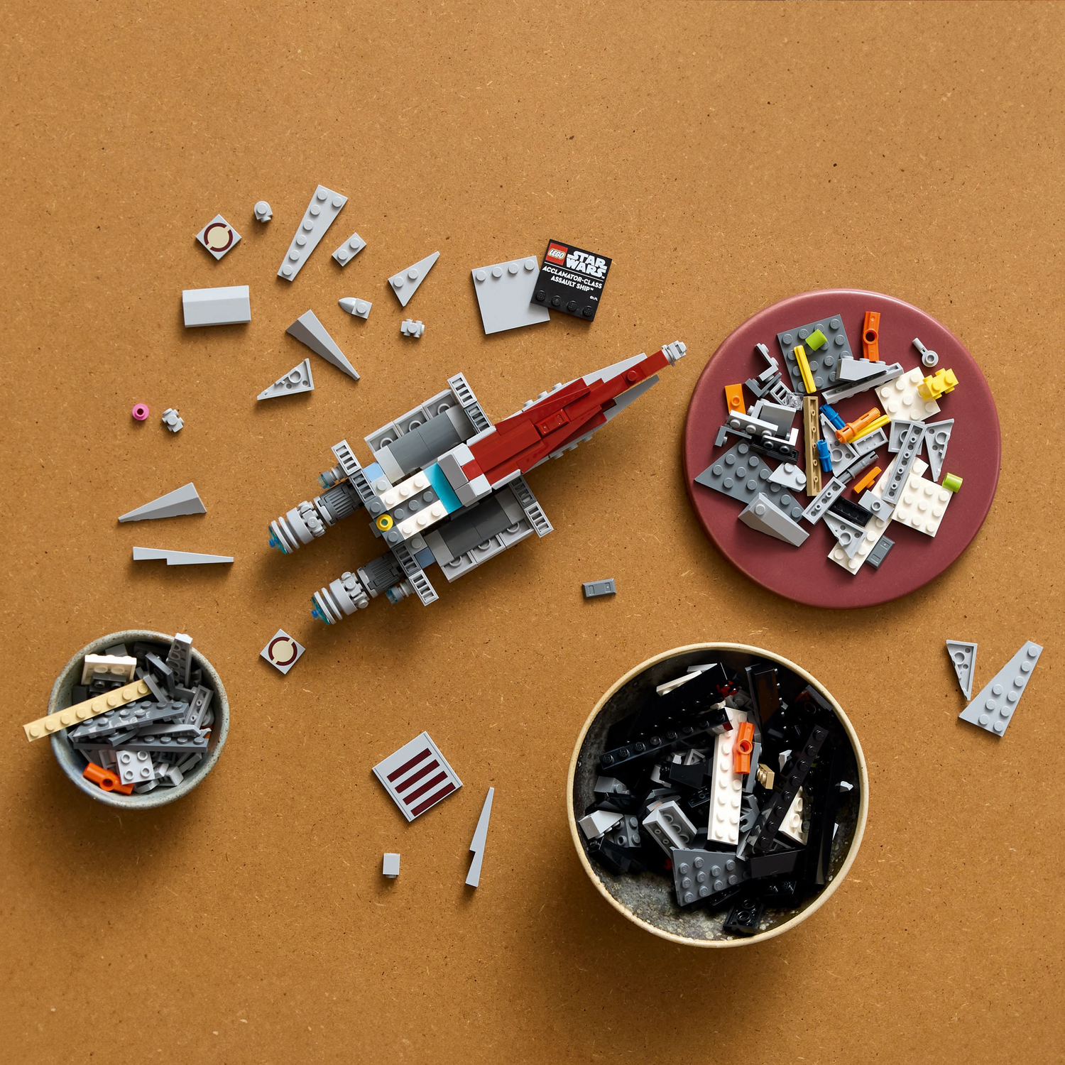 LEGO-stukken voor een rood-grijs Starfighter-model, plus andere stukken in containers en een bord.