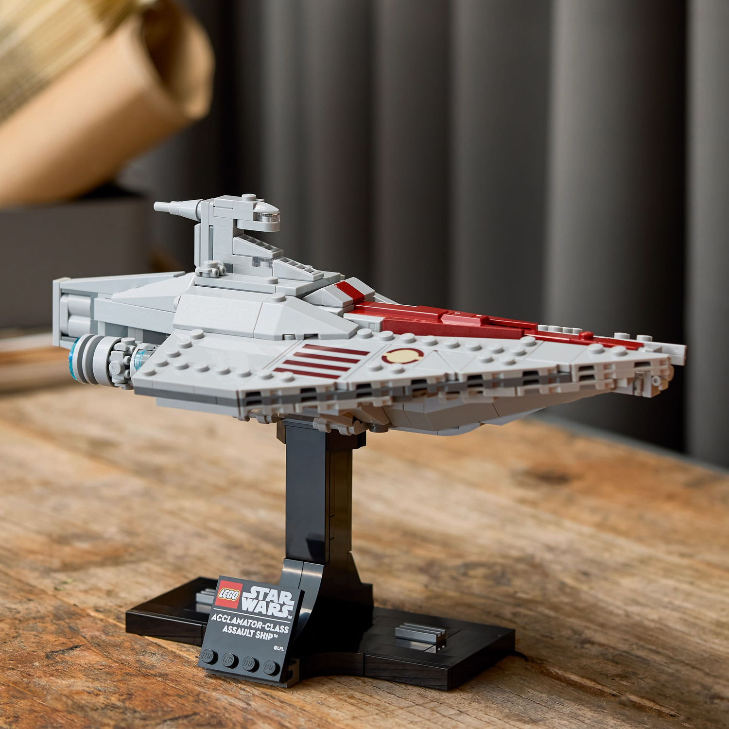 LEGO Acclamator-Class Assault Ship-model, grijs en rood, op een zwarte standaard, op een houten tafel.