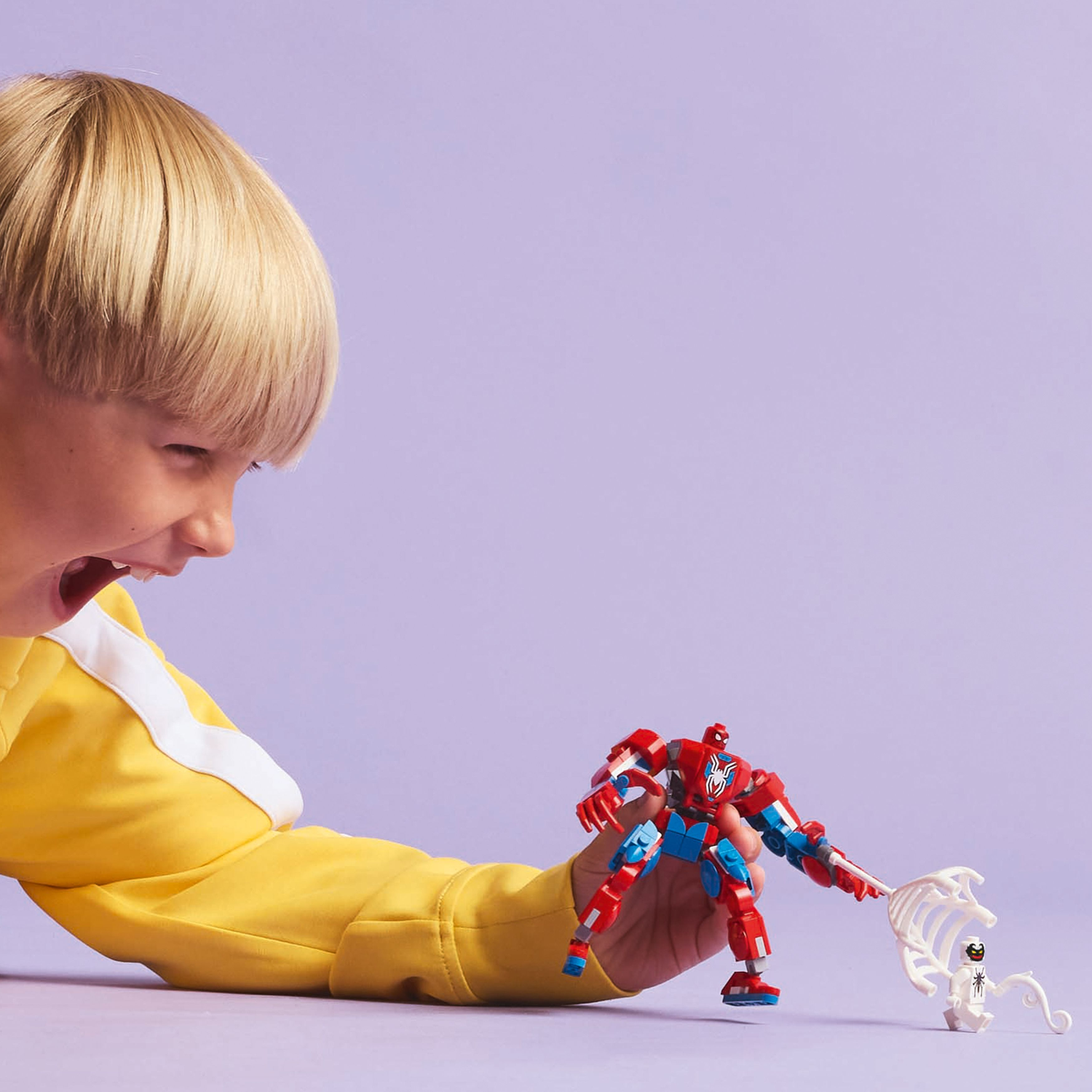 A child is holding a red, white, and blue Spider-Man mech Lego, facing an Anti-Venom figure and web.