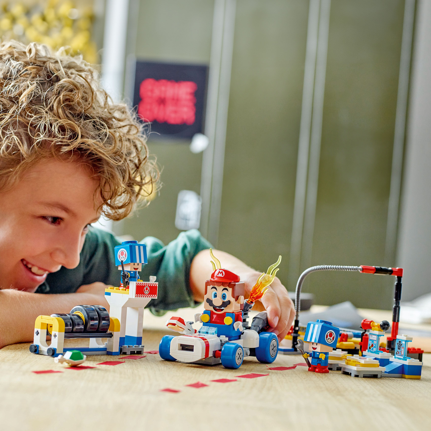 A boy plays with a Lego Super Mario set, featuring a kart and Toad's Garage elements.