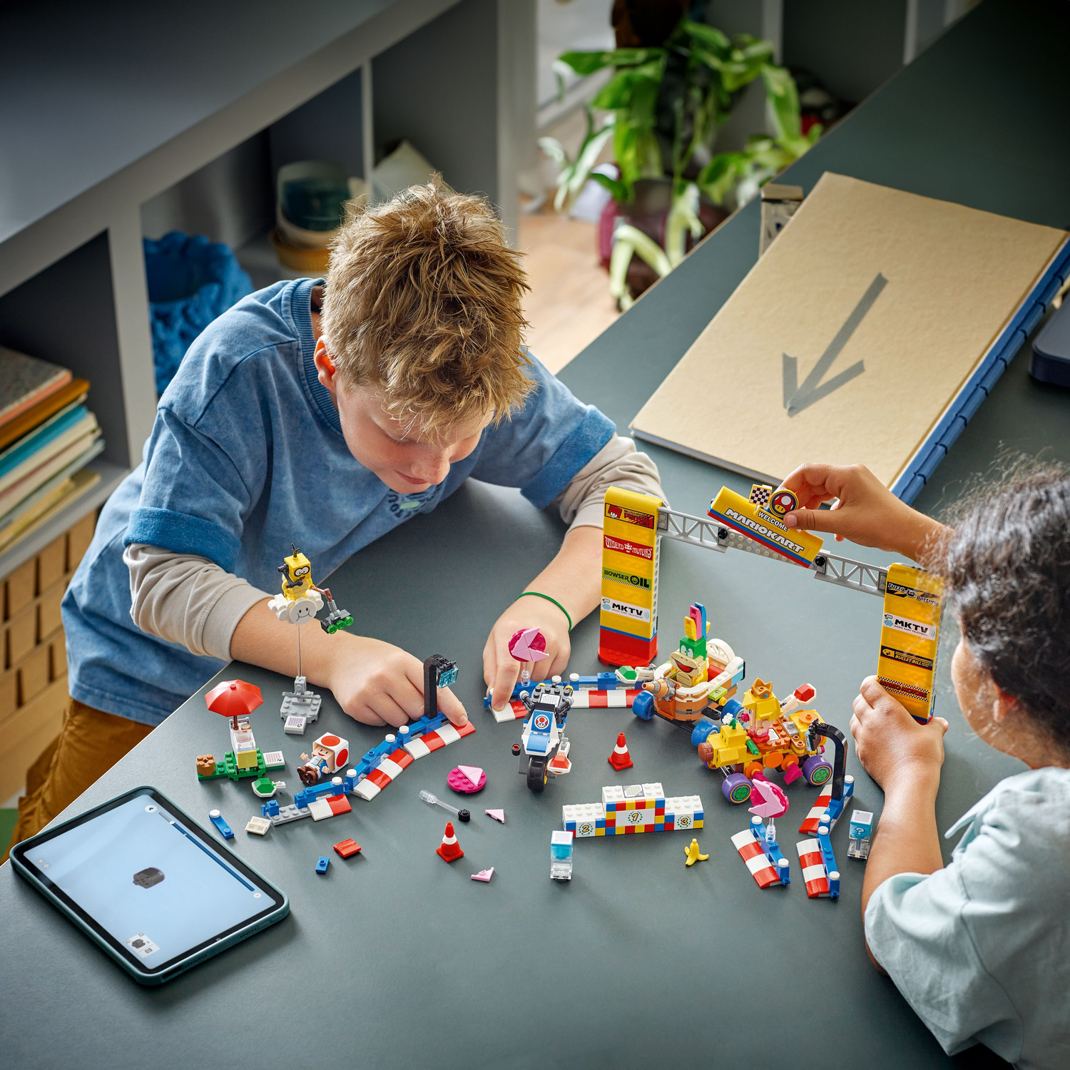 Twee kinderen bouwen een Lego Super Mario set. Een tablet toont de bouwinstructies.