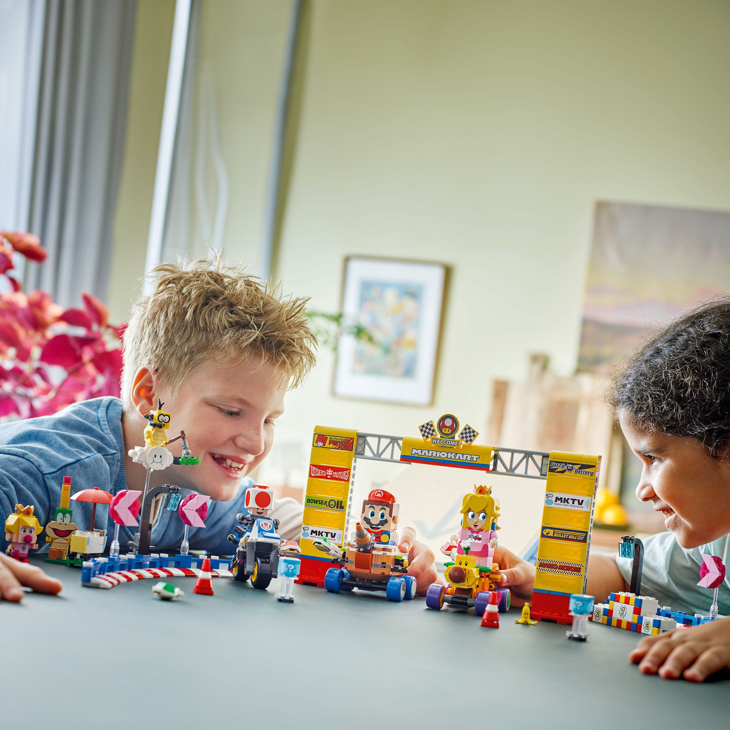 Twee kinderen lachen terwijl ze met een Lego Super Mario set spelen. Mario kart is te zien.