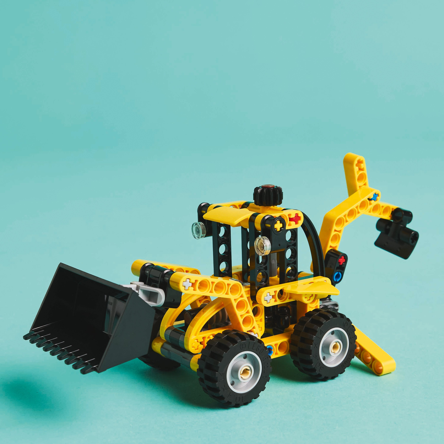 Yellow Lego backhoe loader model on a teal background, detailed view.