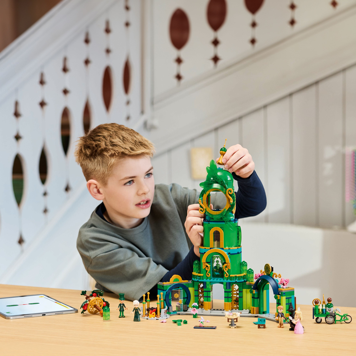 Jongen speelt met Lego set, bouwt een hoge groene toren, met figuren en een bord.