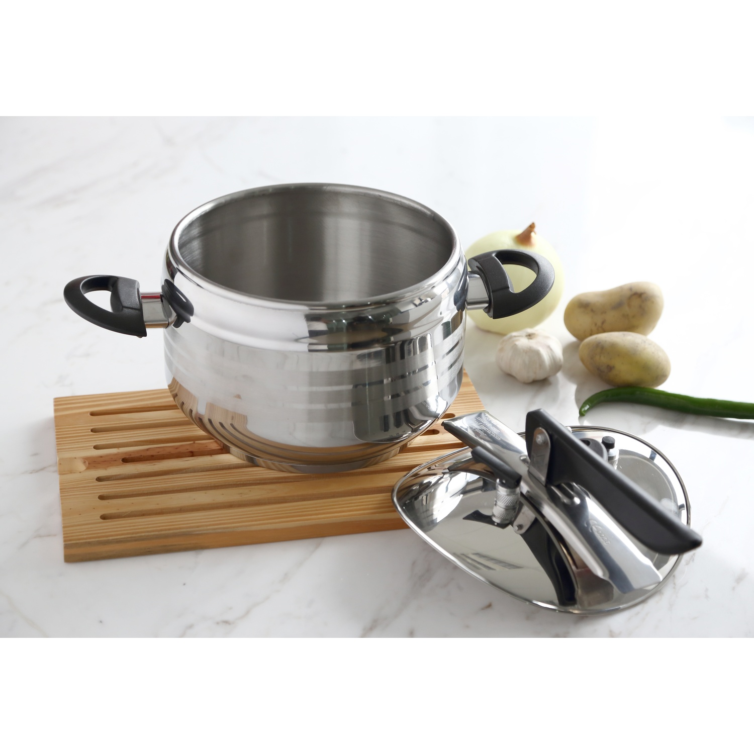 Una pentola a pressione è su un tagliere con verdure. Un cucchiaio di legno è vicino. Lo sfondo è bianco.