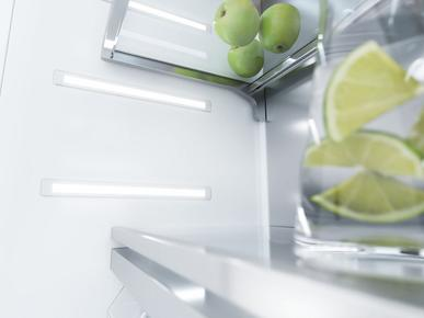 Işıklar ve bir bardak limon ile buzdolabı içi. Üstte yeşil elmalar var.