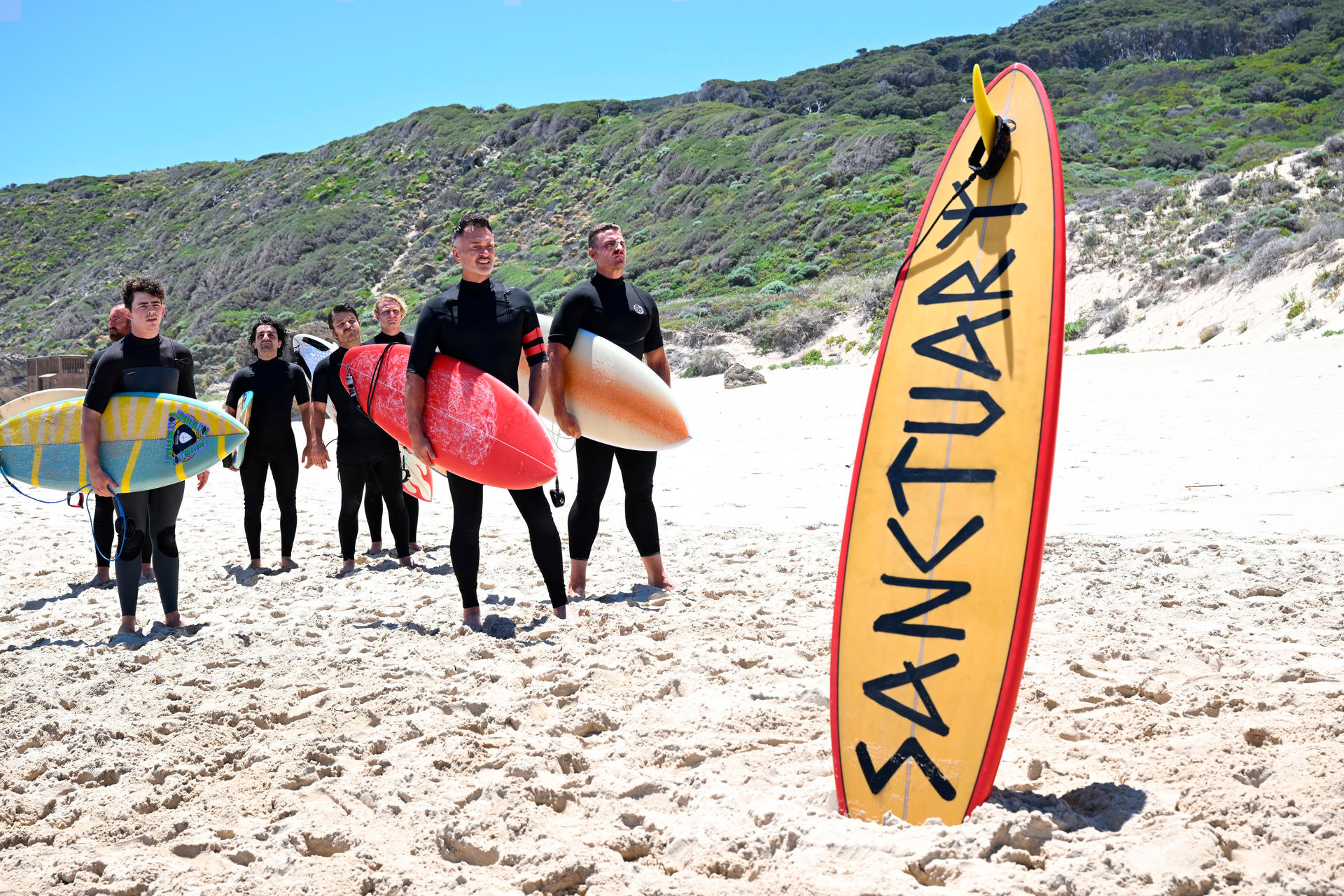 Gruppe von Surfern mit Surfbrettern am Strand. Auf einem Surfbrett steht 'SANTUARK'.
