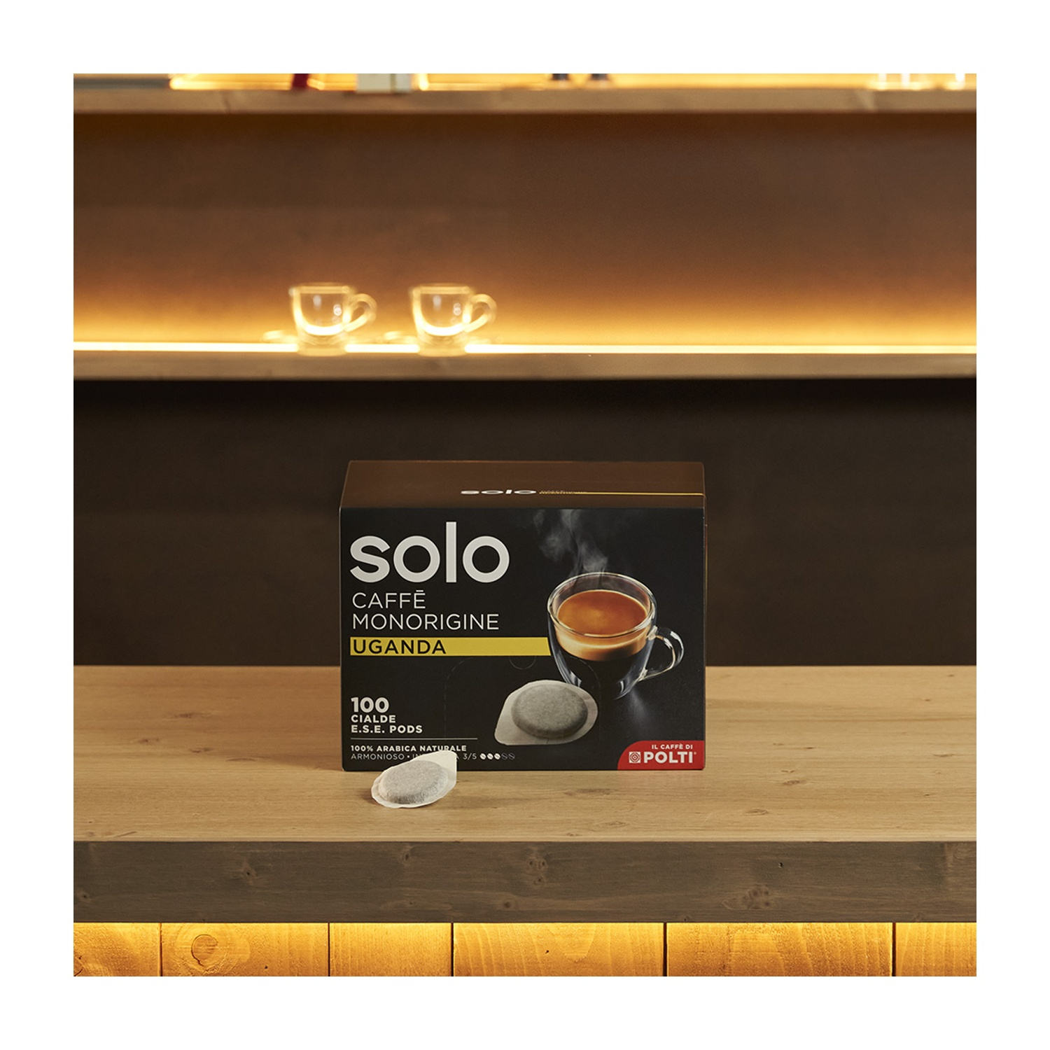 Una scatola di cialde di caffè è su una superficie di legno. Due tazze di caffè sullo sfondo.