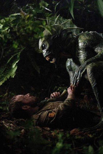 Ein Monster greift einen Mann in einem Wald an. Das Monster ist grün mit spitzen Zähnen. Der Mann liegt am Boden.