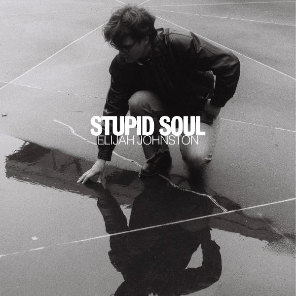 Mann kniet auf nassem Bürgersteig, Kopf gesenkt, Reflexion. Text: STUPID SOUL, ELIJAH JOHNSTON.