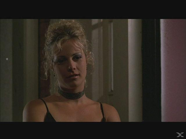 Eine blonde Frau in einem schwarzen Kleid, Choker und dunklem Hintergrund. Sie blickt leicht zur Seite.