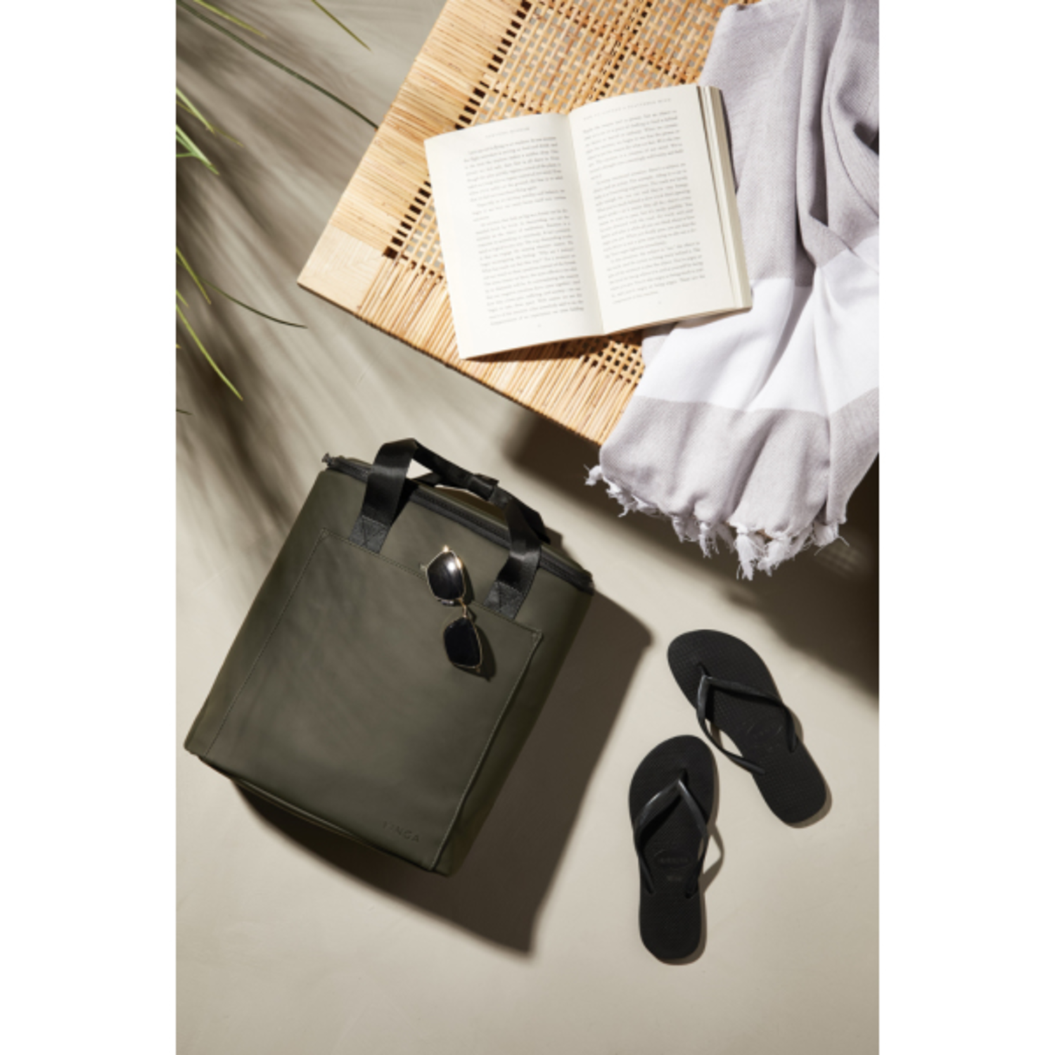 Green cooler bag with sunglasses, flip-flops, book, and towel.