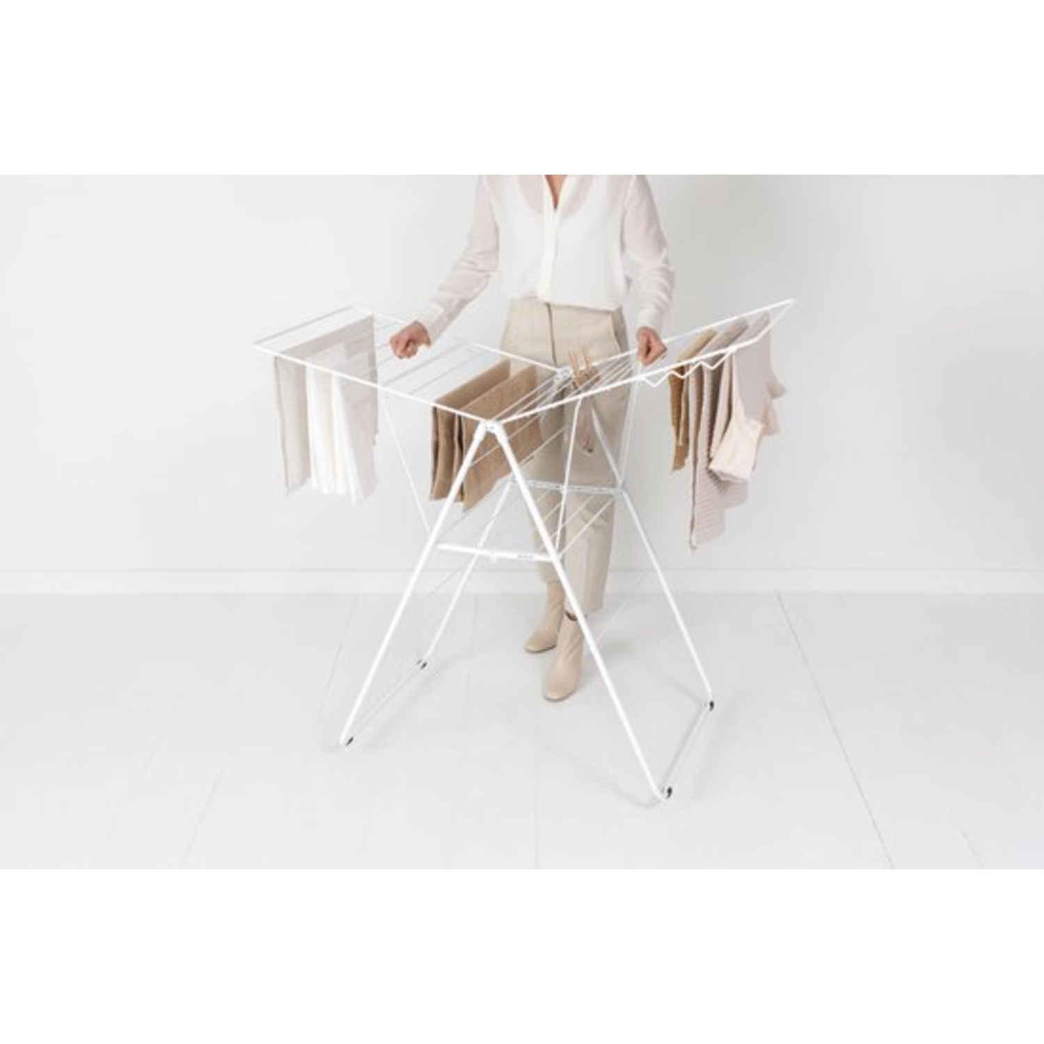 A woman hangs clothes on a white drying rack, set against a white backdrop.